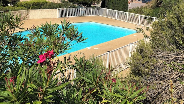 A swimming pool surrounded by greenery and a white fence, with a view of a historic town and hills in the background.
