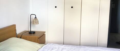 Ein Schlafzimmer mit Bett, Nachttisch, Lampe und Kleiderschrank.