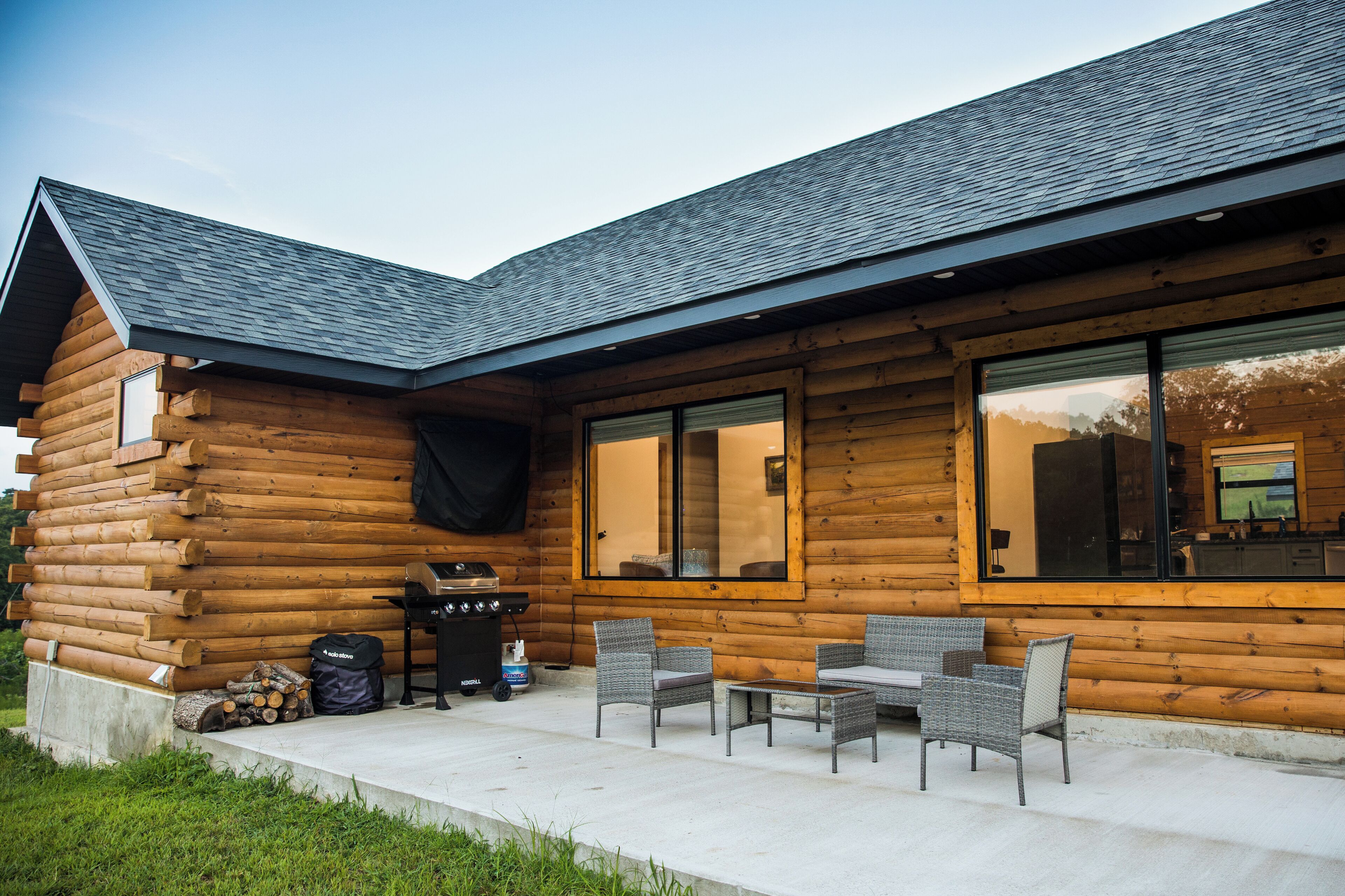 Eine Blockhütte mit einer Terrassenanlage, die Korbmöbel und einen Grill zeigt.