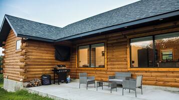 Eine Blockhütte mit einer Terrassenanlage, die Korbmöbel und einen Grill zeigt.