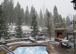 A snow-covered outdoor pool area with lounge chairs and a stone fireplace.