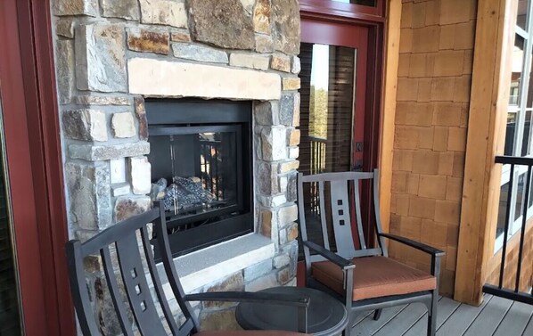 A stone fireplace with a TV, two chairs, and a wooden deck.