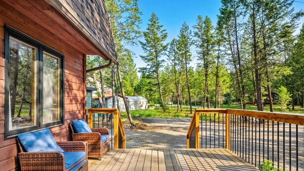 Una terraza de madera con mobiliario de mimbre y vistas a un bosque.