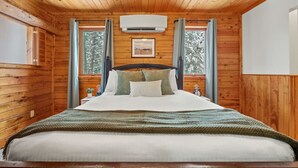 Un dormitorio de cabaña de madera con una cama, una ventana, un aire acondicionado y un cuadro enmarcado en la pared.