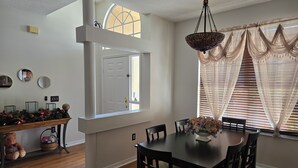Un comedor con una mesa y sillas de madera, un jarrón decorativo y una ventana con cortinas de encaje.