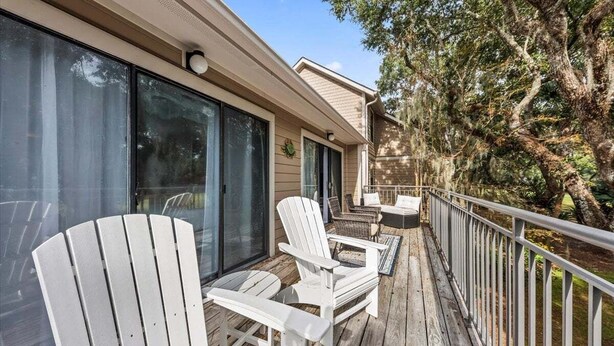 A wooden deck with white Adirondack chairs and a glass door leading to a covered area. - 2nd Floor 1BR/2BA High Hammock Villa! Amenity access NOT permitted (Seabrook Island)