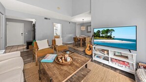 A modern living room with a large flat-screen TV, a wooden coffee table, and a dining area with a guitar. - 2nd Floor 1BR/2BA High Hammock Villa! Amenity access NOT permitted (Seabrook Island)