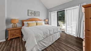 A bedroom with a large bed, two bedside tables, a wooden wardrobe, and a sliding glass door to a balcony. - 2nd Floor 1BR/2BA High Hammock Villa! Amenity access NOT permitted (Seabrook Island)