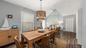 A dining area with a wooden table and chairs, a hanging light fixture, and a large window with blinds. - 2nd Floor 1BR/2BA High Hammock Villa! Amenity access NOT permitted (Seabrook Island)