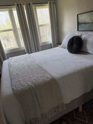 A neatly made bed with a quilted bedspread and a throw blanket, positioned next to a window with curtains.