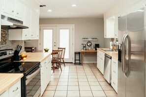 A modern kitchen with white cabinets, a stainless steel refrigerator, a wooden dining table, and a coffee maker.