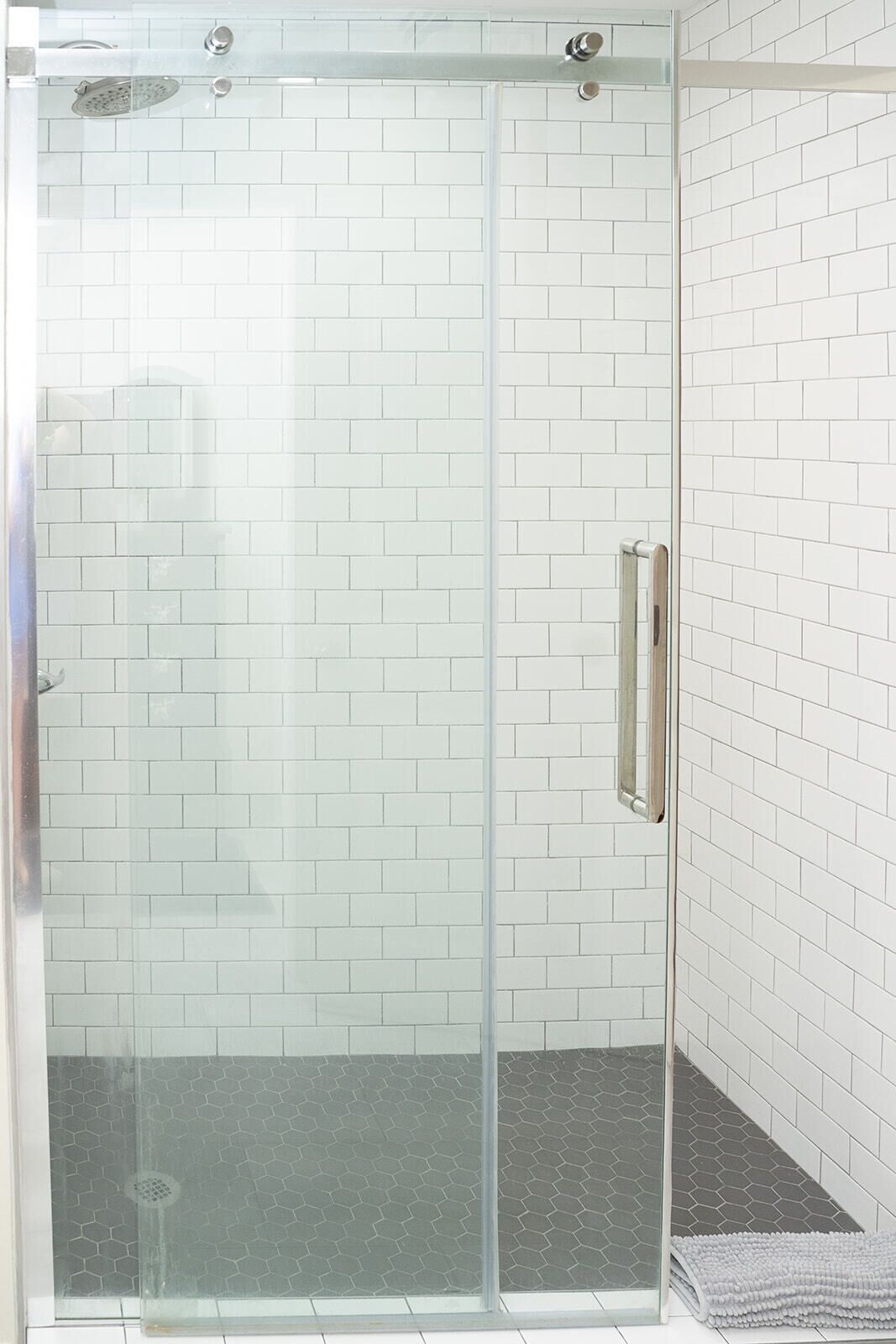 Ducha envuelta en vidrio con azulejos tipo metro blancos y un pomo metálico.