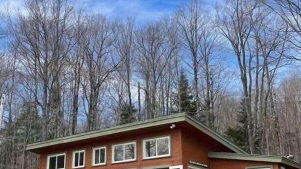 Une cabane en bois à deux étages, dotée d’un balcon et entourée d’arbres.