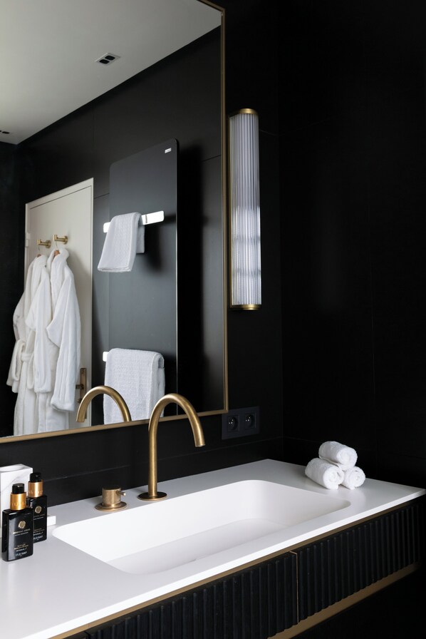A modern bathroom with a large mirror, a white sink, gold fixtures, and neatly arranged towels. - HIGHSTAY - Luxury Serviced Villa - Poincaré (Paris)