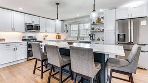 A modern kitchen with white cabinets, stainless steel appliances, and a central island with bar stools.