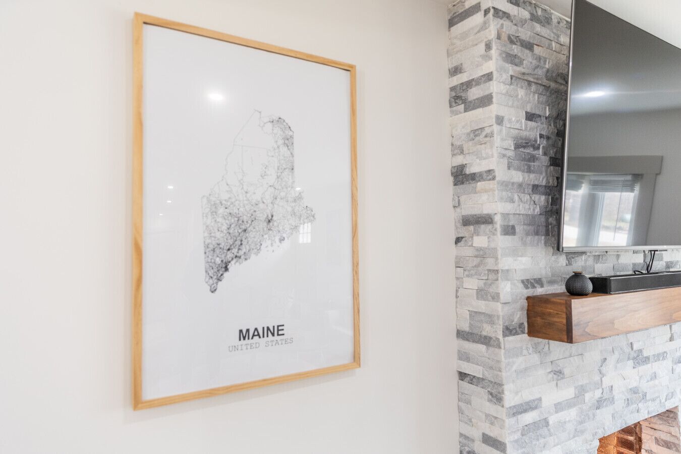 A framed map of Maine, USA, mounted on a white wall.