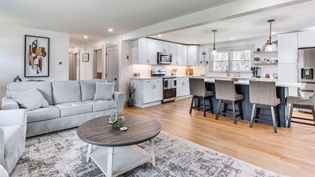 A modern living room with a grey sofa, a coffee table, and a kitchen area with white cabinets and a central island.