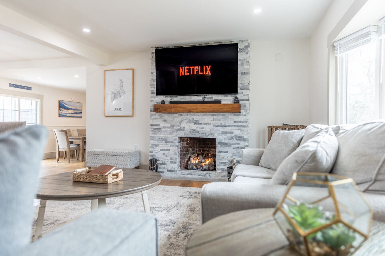 Een moderne woonkamer met een stenen open haard, een aan de muur bevestigde televisie waarop 'NETFLIX' staat, en een gezellige zithoek.