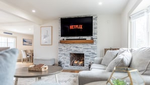 A modern living room with a stone fireplace, a mounted television displaying 'NETFLIX', and a cozy seating area.