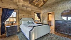 Un dormitorio de cabaña de madera con una cama, mesitas de noche, cómoda y ventilador de techo.