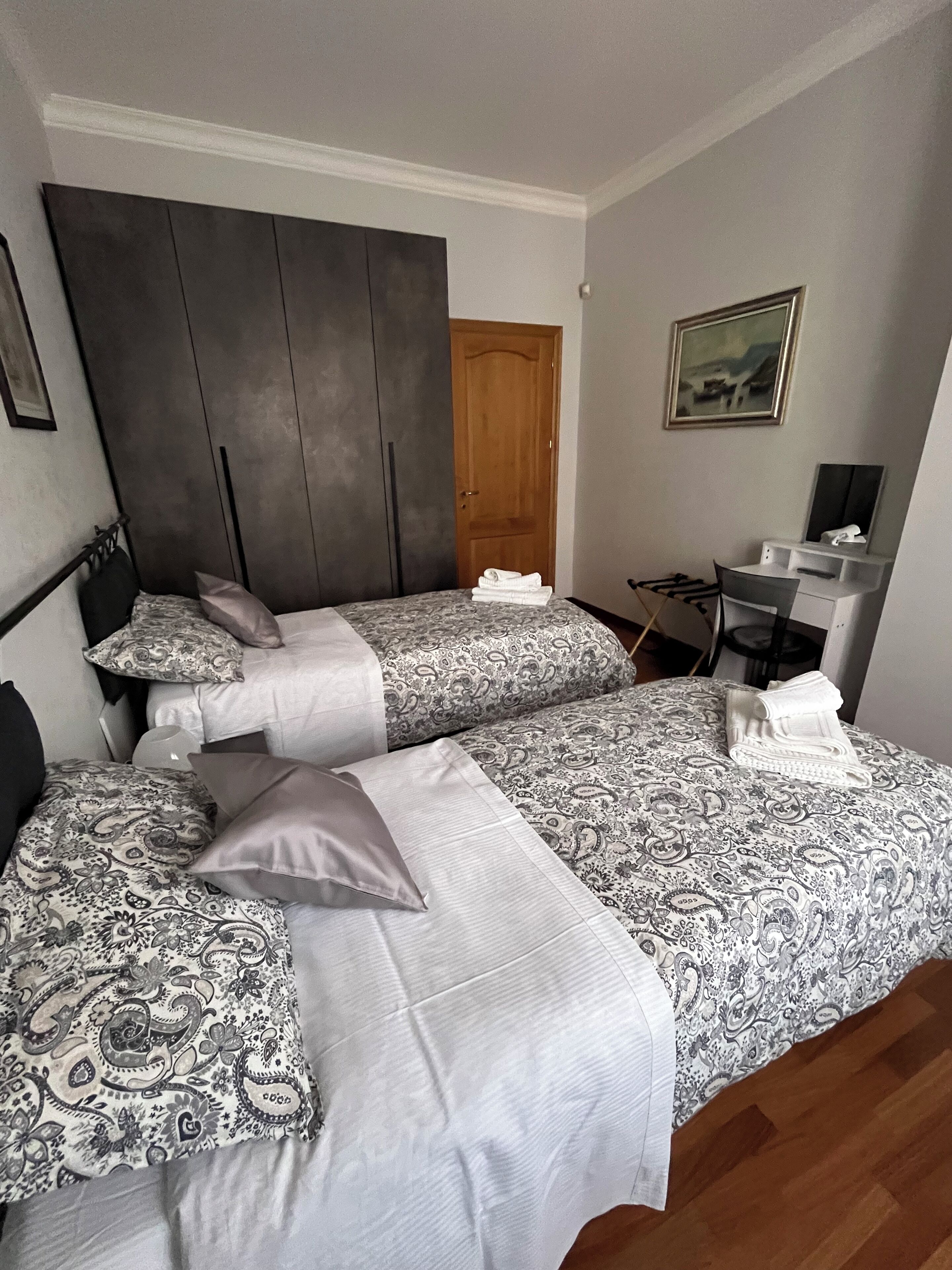 Ein Schlafzimmer mit zwei Betten, einem Kleiderschrank, einem Schreibtisch und einem Bild an der Wand.