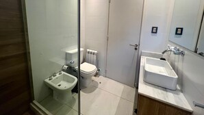 Un baño moderno con cabina de ducha de vidrio, un bidé, un inodoro y un lavamanos.