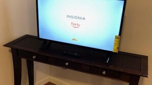 Un televisor sobre un mueble bajo de madera oscura, con un control remoto, mostrando el logotipo 'INSIGNIA' y la marca 'firetv'.
