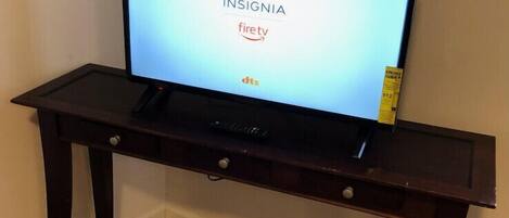 A television on a dark wooden TV stand with a remote control, displaying the 'INSIGNIA' logo and 'firetv' branding.