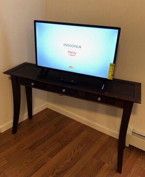 Un téléviseur posé sur un meuble TV en bois foncé, avec une télécommande à proximité, affichant le logo « INSIGNIA » et la marque « firetv ».