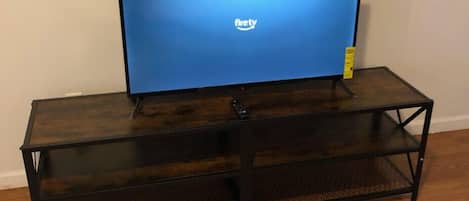 A flat-screen TV on a wooden TV stand with a mesh shelf.