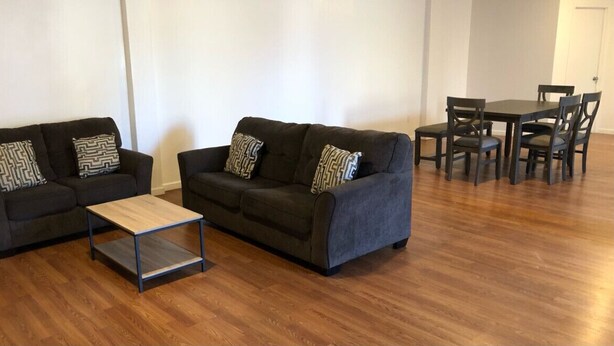 Una sala de estar con dos sofás oscuros, una mesa de centro de madera y una mesa de comedor con sillas.