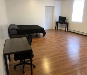 A room with a bed, a desk, and a chair. There is a door and a window.