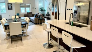 Una cocina moderna con un refrigerador de acero inoxidable grande, una isla central con taburetes y un comedor con mesa y sillas.