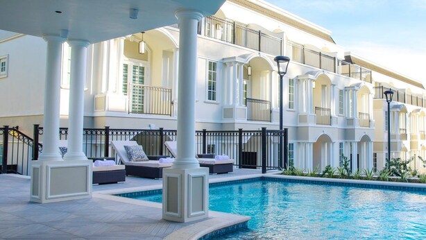Un área de piscina con piscina blanca, sillas de descanso y un edificio con balcones.