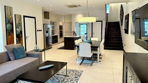 Una cocina moderna con una isla central, un comedor con una escalera y una sala de estar con sofá y mesa de centro.