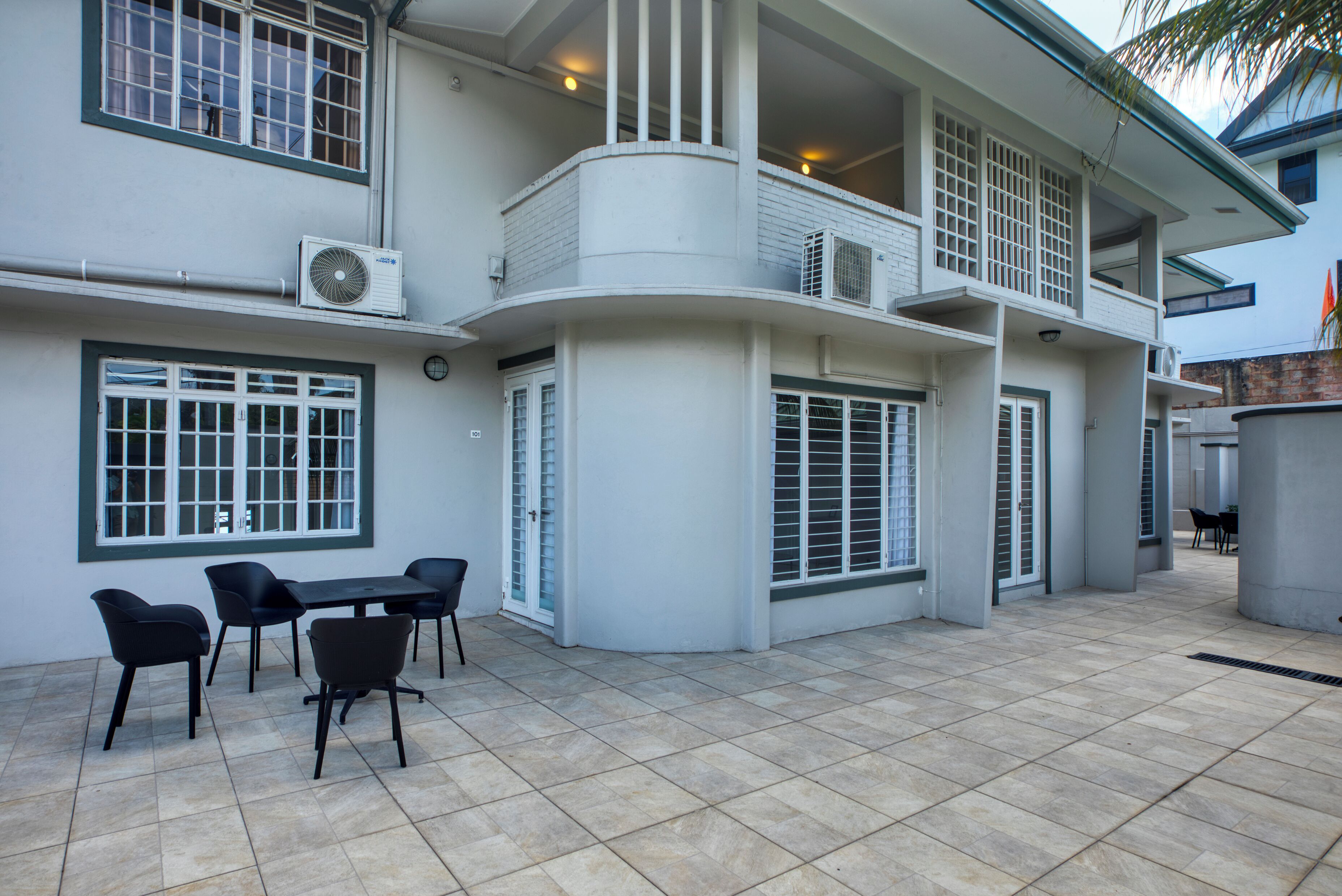 A modern building with multiple balconies, large windows, and a tiled patio area with outdoor seating.