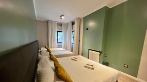 A bedroom with a large bed, a bedside table, a window with curtains, and a radiator. - Quadruple Room with Private External Bathroom (Mendoza)