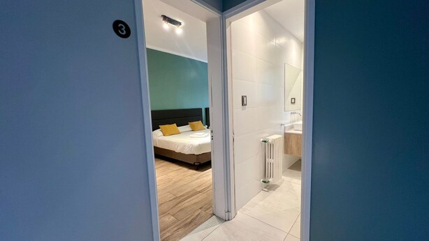 A modern hotel room with a bed, a bathroom, and a view of the hallway. - Quadruple Room with Private External Bathroom (Mendoza)