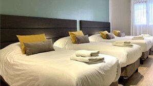 A hotel room with three beds, each with white bedding and multiple pillows. - Quadruple Room with Private External Bathroom (Mendoza)