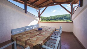 An outdoor patio with a table and chairs, a view of green hills, and a wooden roof structure.