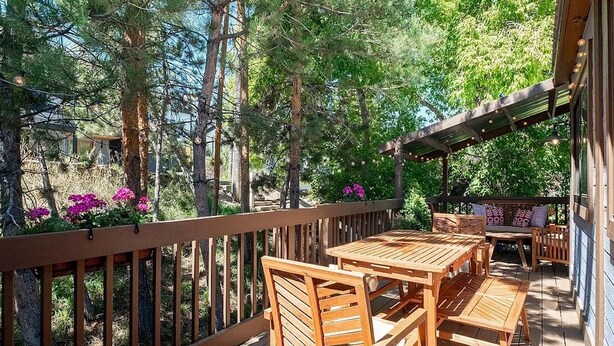 A wooden deck with a table and chairs, surrounded by trees and a wooden railing.