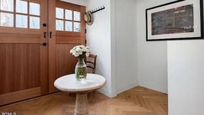 A wooden door with glass panels, a round table with a vase of flowers, and a framed picture on the wall.