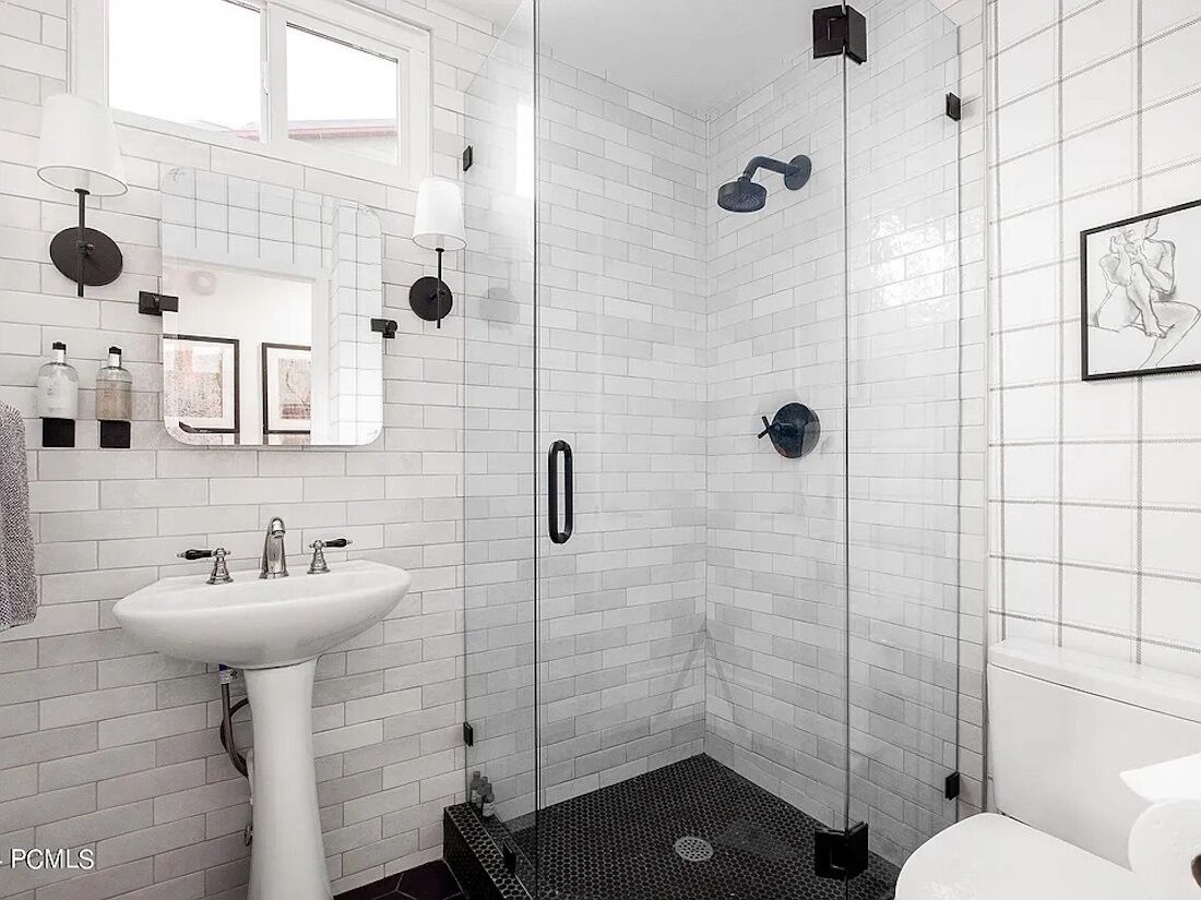 Un baño moderno con ducha revestida de azulejos blancos tipo metro, lavamanos pedestal y un cuadro en la pared.