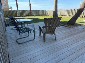 Una terraza de madera con una mesa y sillas, rodeada por un cerco de madera y un jardín con césped.