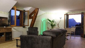 A cozy living room with a sofa, a wooden cabinet, and a television. There is a window with a view of mountains. - Spacious apartment with magnificent view and terrace, on the 1st floor of a villa. (EMBRUN)
