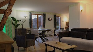 A living room with a sofa, a table, and a chair. There is a dining table with chairs and a clock on the wall. - Spacious apartment with magnificent view and terrace, on the 1st floor of a villa. (EMBRUN)