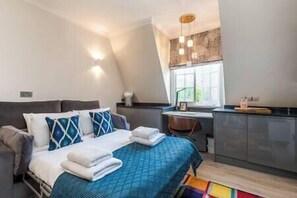 A bedroom with a bed, a desk, and a window. - PBC | Studio Apartment by Sloane Square - FDP (London)