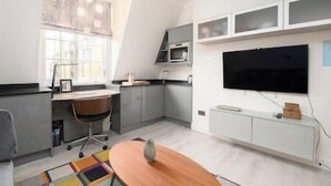 A modern kitchen with a dining area, a large window, and a flat-screen TV mounted on the wall. - PBC | Studio Apartment by Sloane Square - FDP (London)