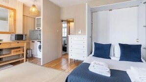 A bedroom with a bed, a dresser, a microwave, and a washing machine.