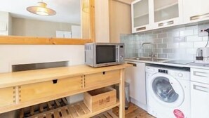 A compact kitchen with a microwave, washing machine, and wooden storage unit.